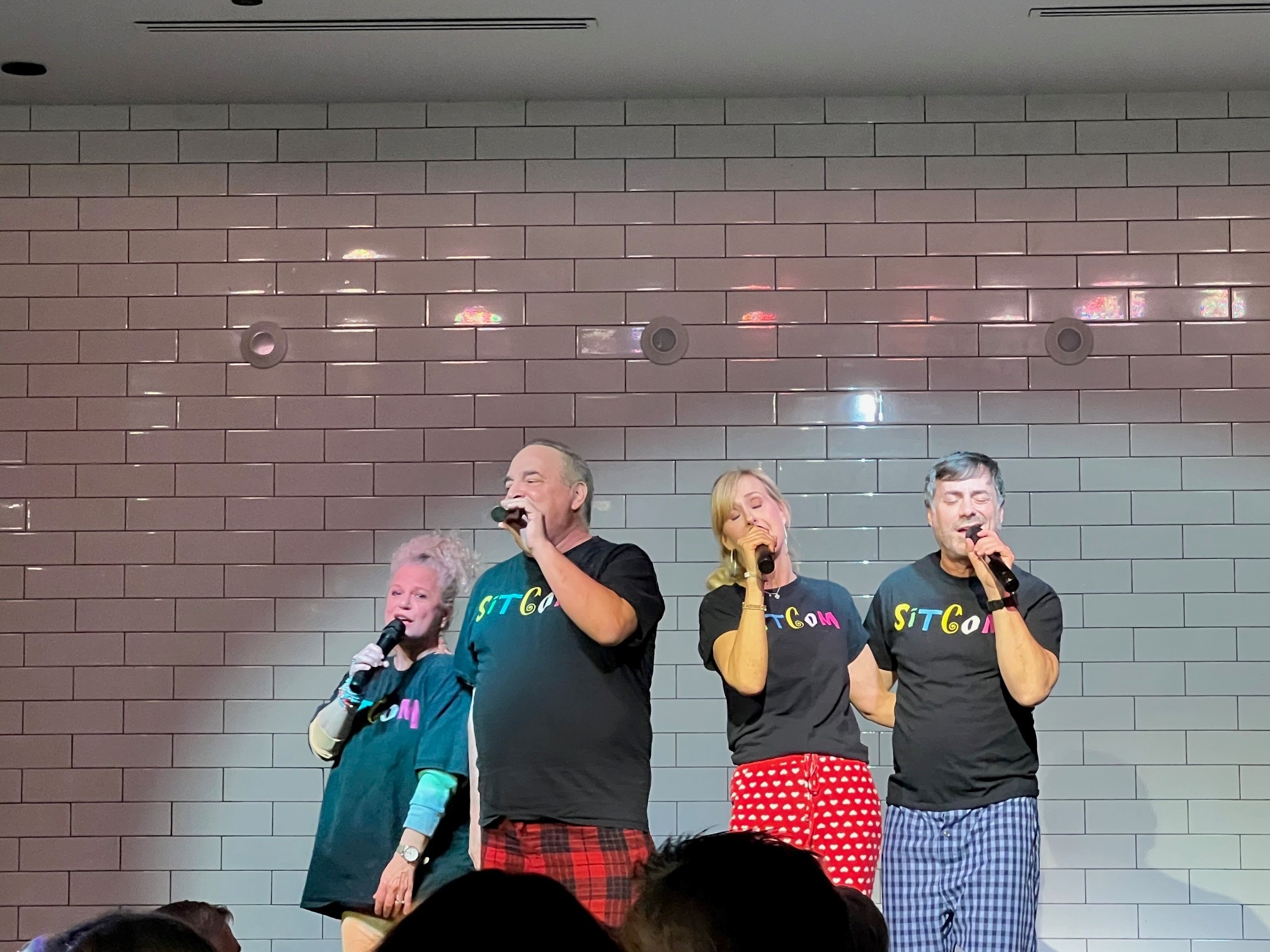 two men and two women singing on a stage, wearing black shirts that read "sitcom"