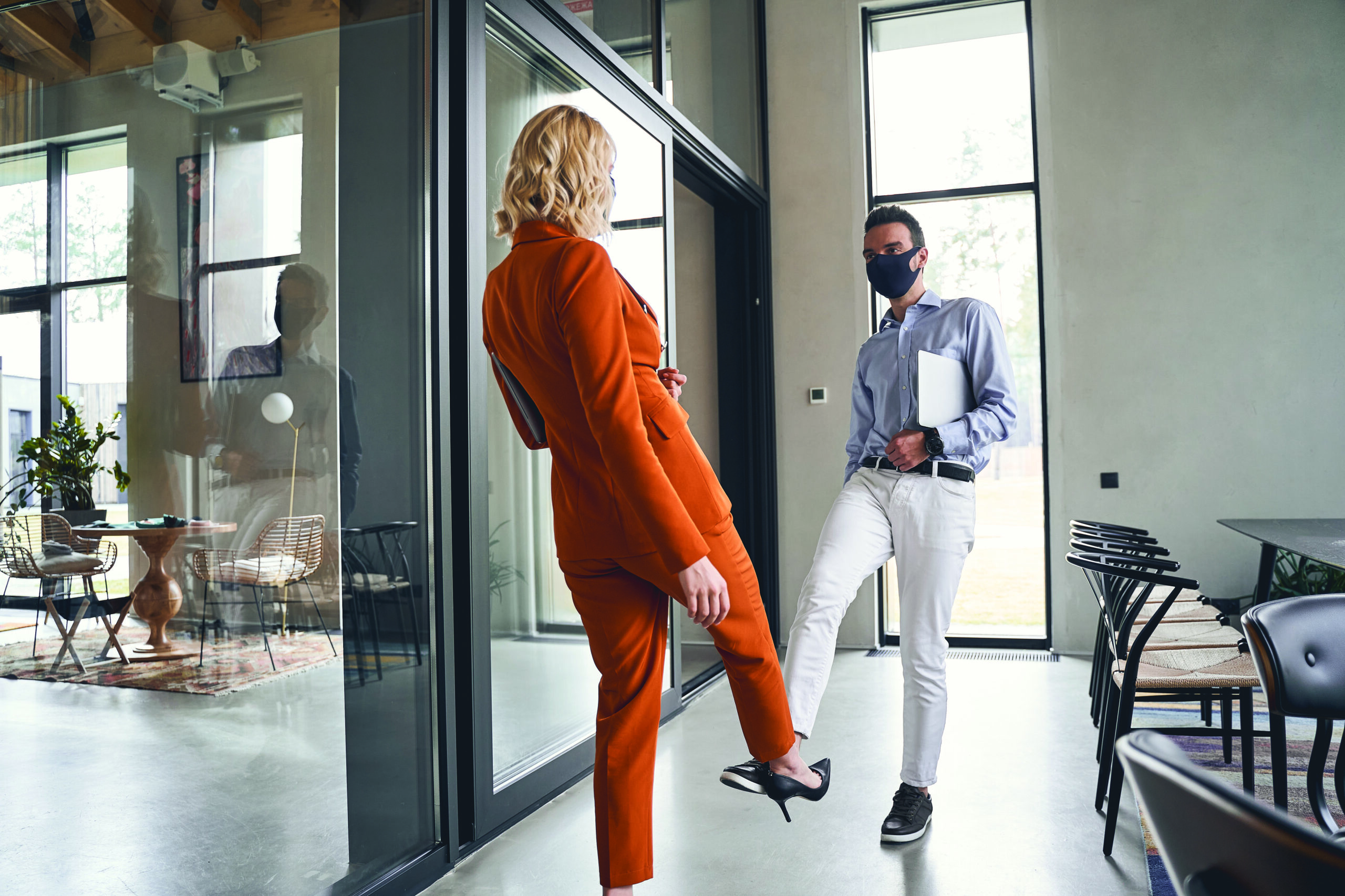 Two people wearing masks touching heels as a greeting. 