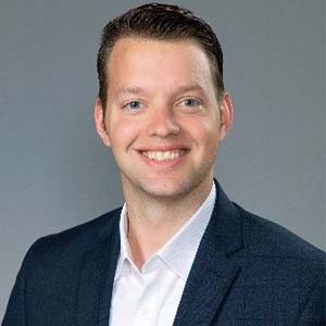 A portrait of Adam Gollub. He is a white man with combed brown hair and a blue jacket
