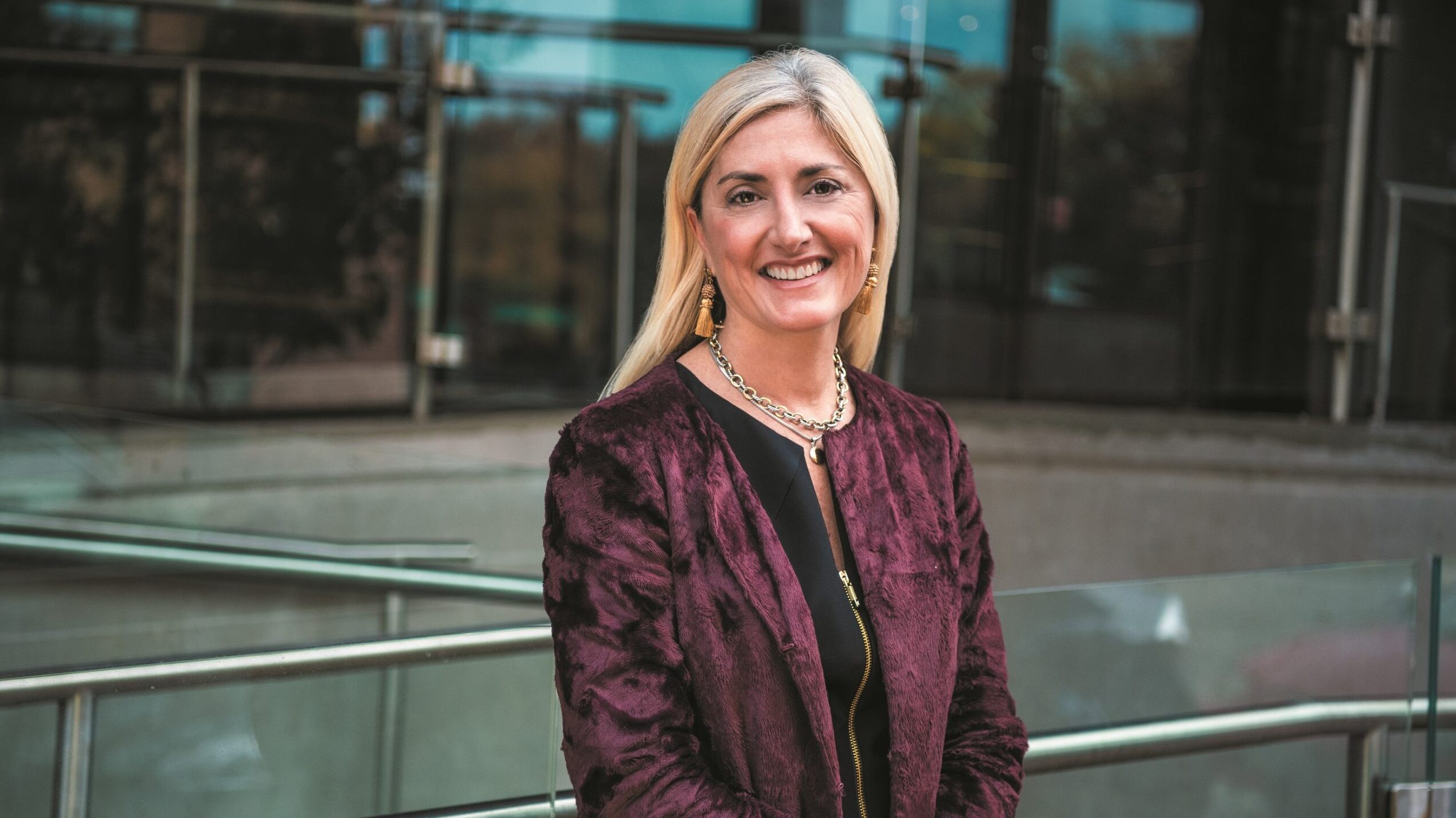 A portrait of Amy Calvert. She is a blonde white woman with a red plaid suit jacket