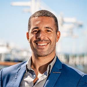 A portrait of Anthony Mancuso. He is a black man with a stubbled beard and a blue suit