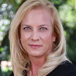 A portrait of Ariane Hiltebrand. She is a blonde white woman with straight hair and a black blouse