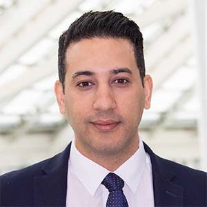 A portrait of Ben Zarhoud. He is a brown man with combed black hair and a blue suit
