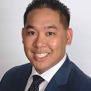 A portrait of Edward Diano. He is a South Asian man with combed black hair and a blue suit