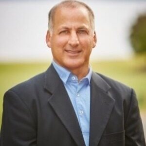 A portrait of Richard Keurajian. He is a balding brown man with a dark jacket