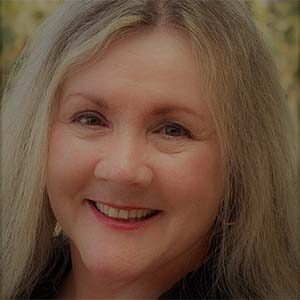 A portrait of Sue Stemley. She is an older white woman with light hair and golden earrings