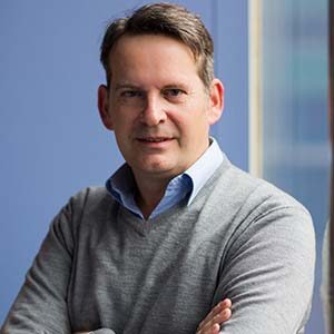 A portrait of Tony Melis. He is a white man with combed greying hair and a grey sweater