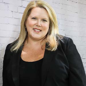 A portrait of Amy Manzanares. She is a white woman with straight blonde hair and a black suit jacket
