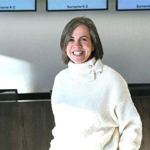 A portrait of Anna Clover. She is a white woman with short greying hair and a white turtleneck sweater