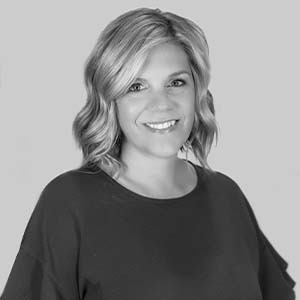A black and white portrait of Annie Gingrich. She is a white woman with short wavy hair and a black blouse