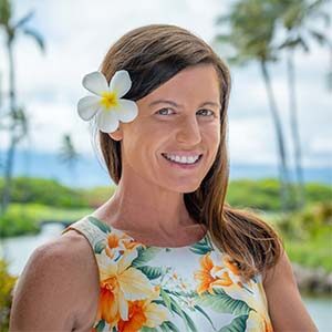 A portrait of Carrie Bligh. She is a white woman with brown hair and a tropical patterned dress