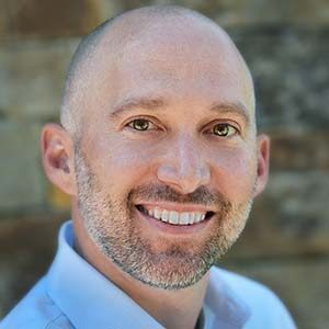 A portrait of Chris Cofelice. He is a balding white man with a stubbled beard and blue collared shirt