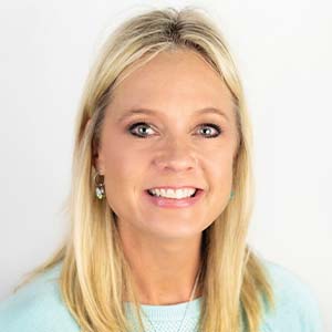 A portrait of Dana Chorpenning. She is a blonde white woman with long hair and a pale blue sweater