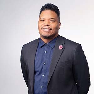 A portrait of Dedren Bailey. He is a black man with short natural hair and a grey suit