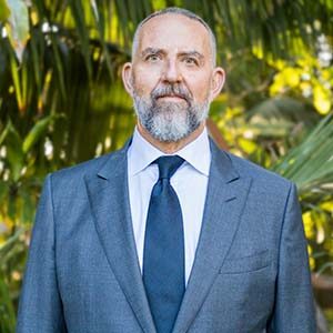 A portrait of Matthew Adams. He is an older brown man with a grey beard and a blue suit