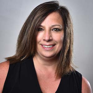 A portrait of Melissa Soto. She is a white woman with straight brown hair and a sleeveless black blouse