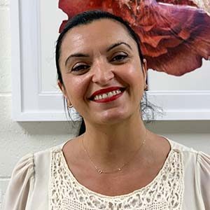 A portrait of Mina Dipalma. She is a brown woman with black hair in a ponytail and a lacy white blouse