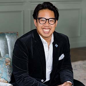 A portrait of Pawin “P.J.” Souksanith. He is an Asian man with medium-length black hair and a black suit