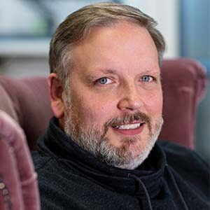 A portrait of Tim Collett. He is a white man with combed greying hair, a stubbled beard and a sweatshirt