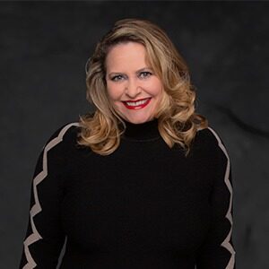 A portrait of Amy Arbuckle. She is a white woman with loosely curled blonde hair and a black blouse.