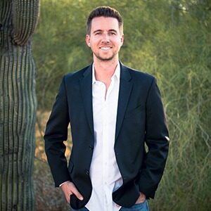 A portrait of Ryan Kirby. He is a white man with a dark suit jacket and jeans.