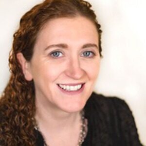 A portrait of Deborah Tappan. She is a white woman with red curly hair and a black blouse.