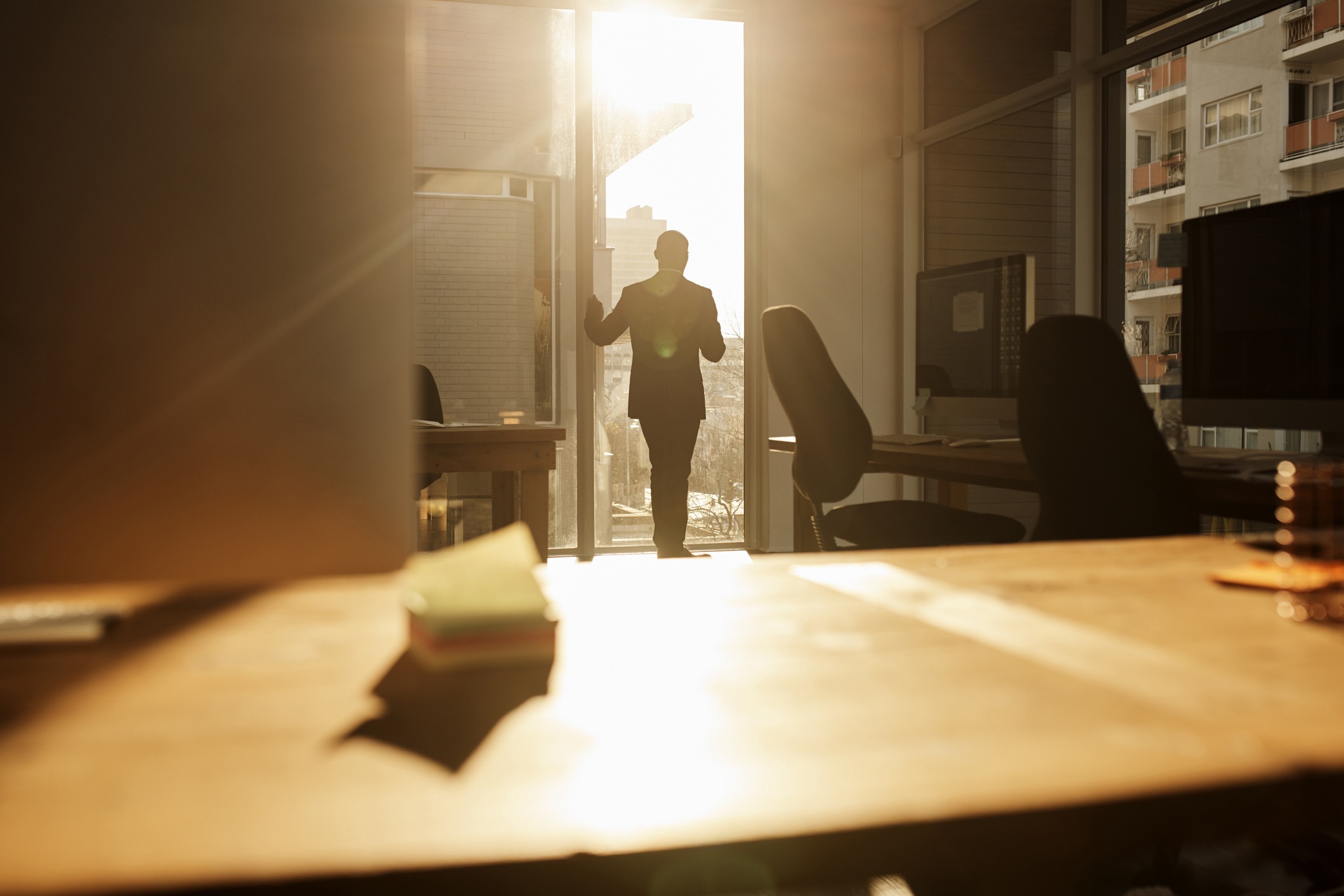 A person in a suit is opening a door to look at a desk.