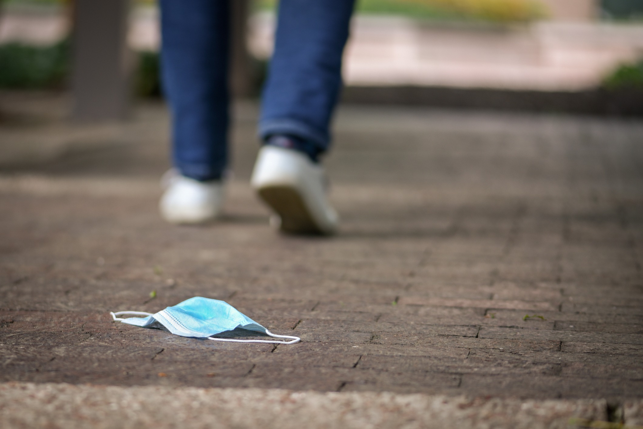 A person walking away from a mask on the ground.