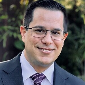 A portrait of Alex Batista. He is a white man with dark hair and square glasses.