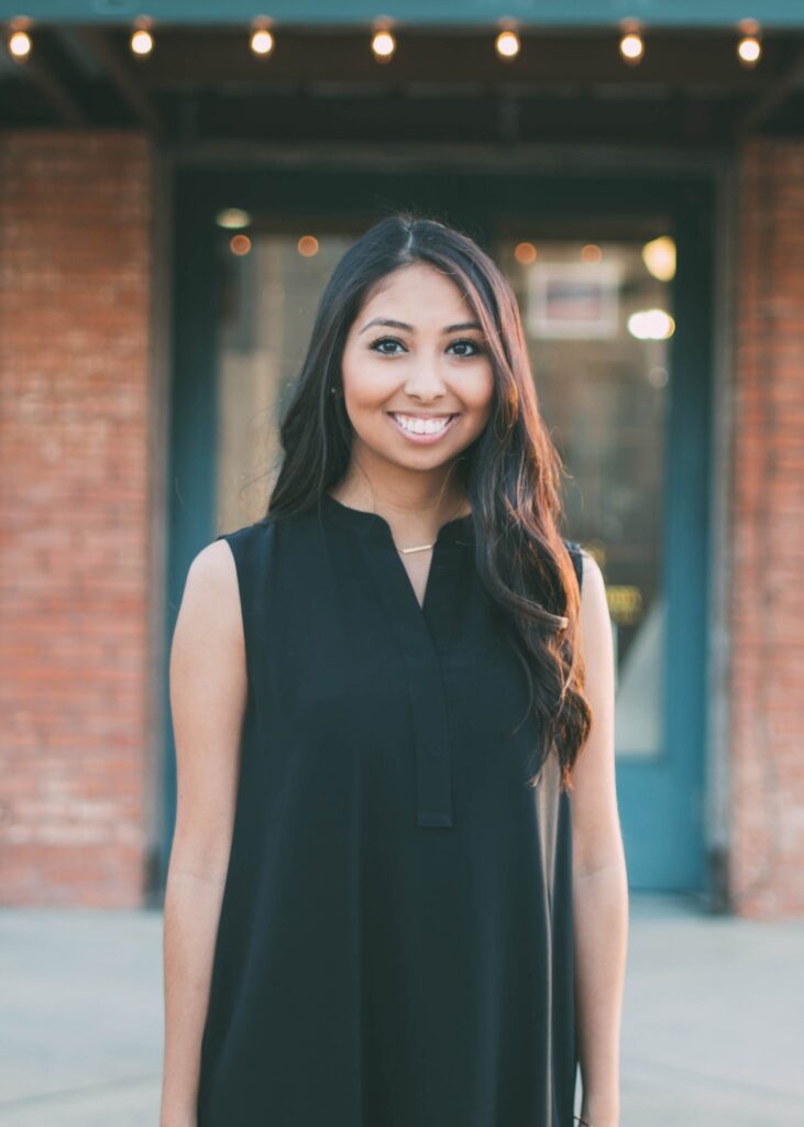 A portrait of April Brown, a young south Asian woman with dark, loosely curled hair and a black dress.