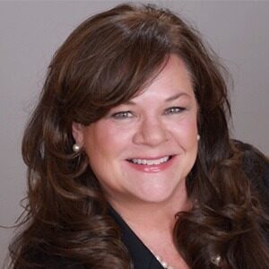 A portrait of Colleen Hughes. She is a white woman with loosely curled brown hair and pearl earrings.
