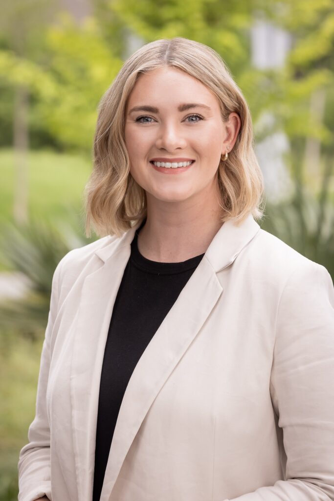 A portrait of Kaitlyn Grekoff, a young white woman with short blond hair and a light pink suit jacket.