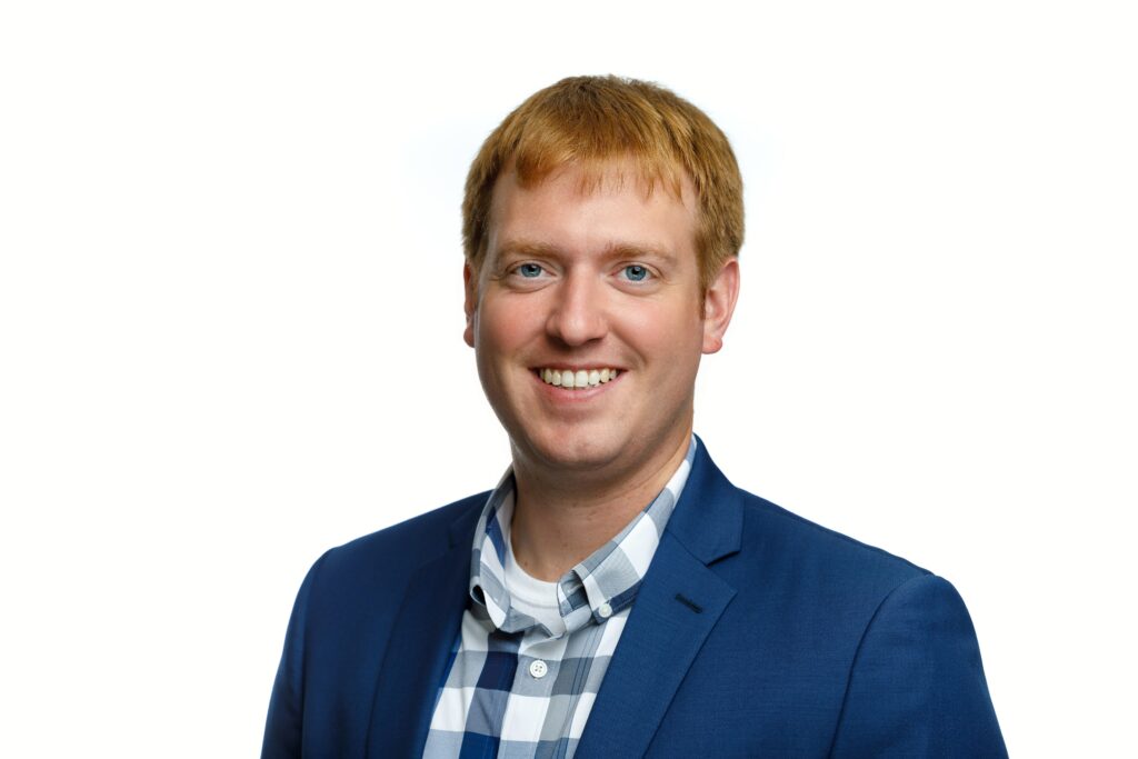 A portrait of Nick Kleva, a young white man with red hair and a blue suit jacket.