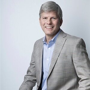 A portrait of Phillip Allen. He is an older white man with greying hair and a tan plaid suit.