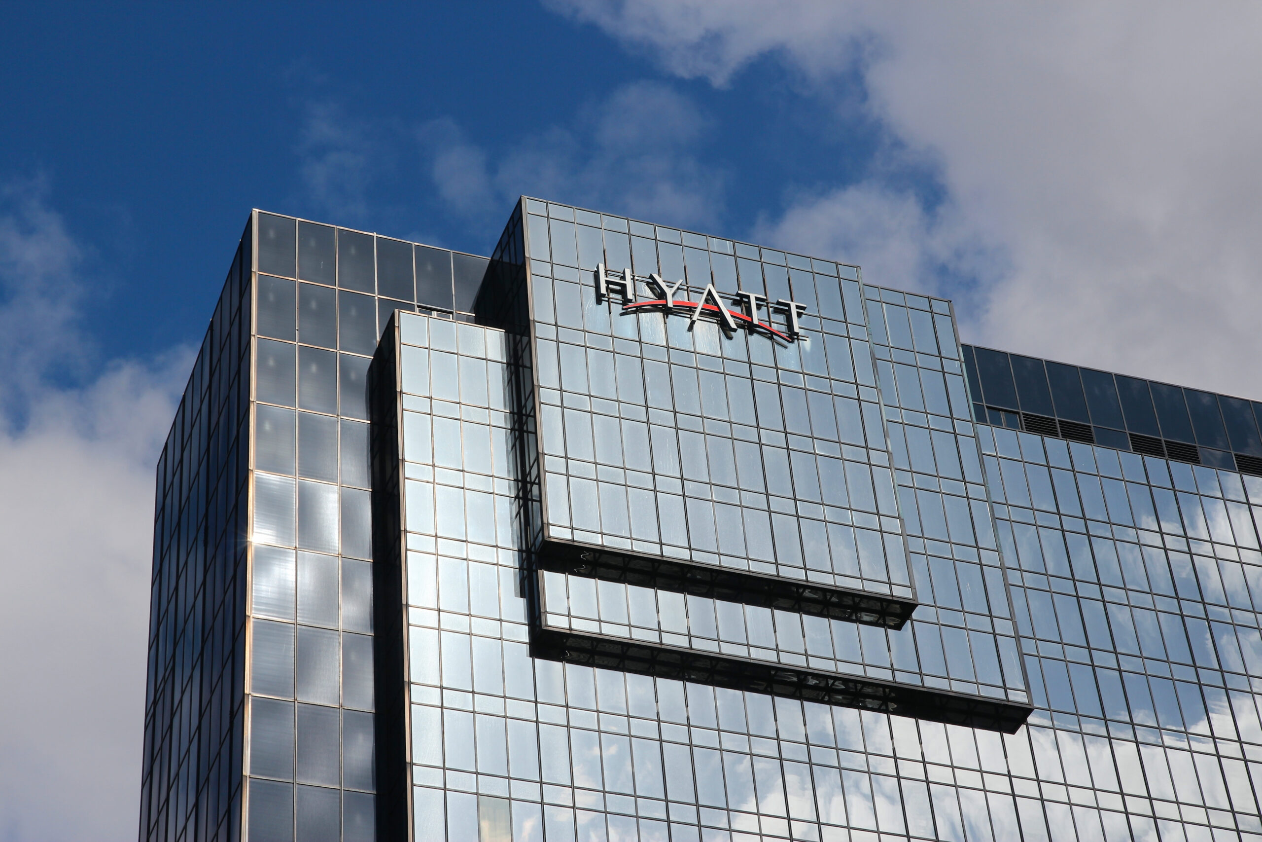 The side of the Hyatt building in the UK. It has reflective windows showing a lightly cloudy sky.