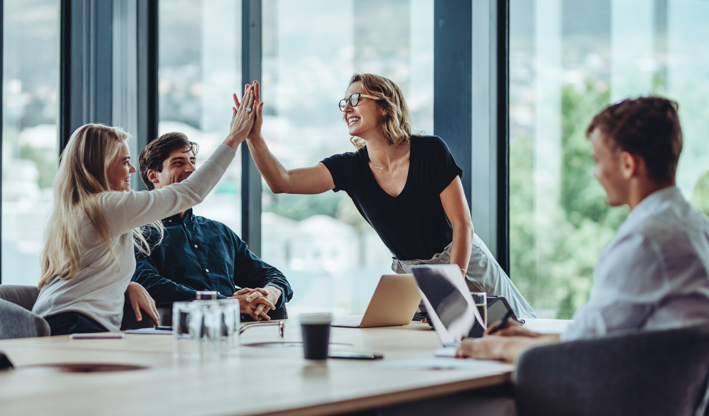Two women giving each other a high five at a meeting table.