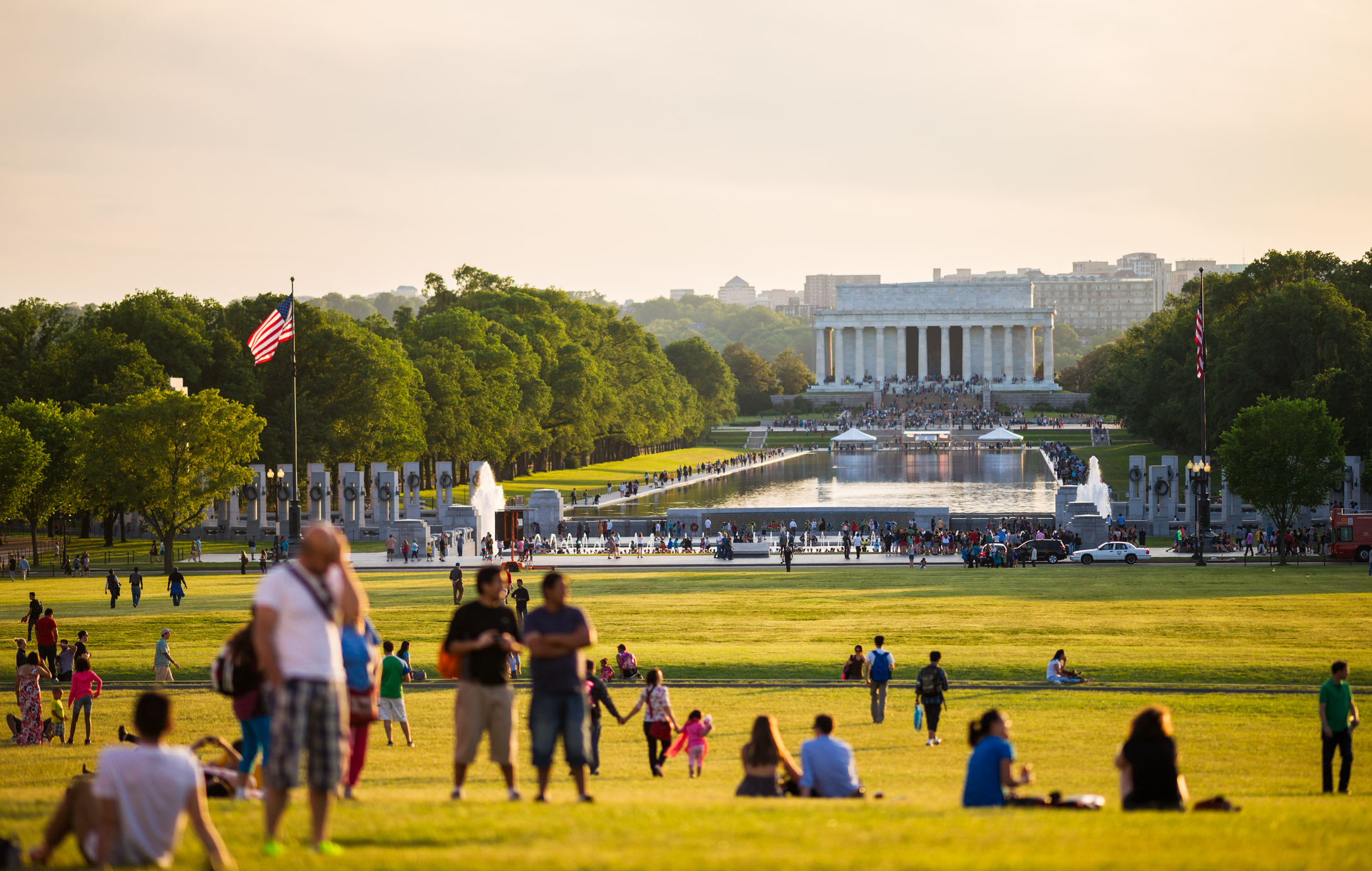 A group of tourists on the lawn across the pool from the Lincoln Memorial.