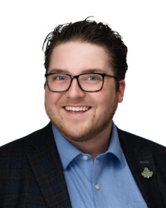 A portrait of Tyler Cole, a young white man with square glasses and a black suit jacket.