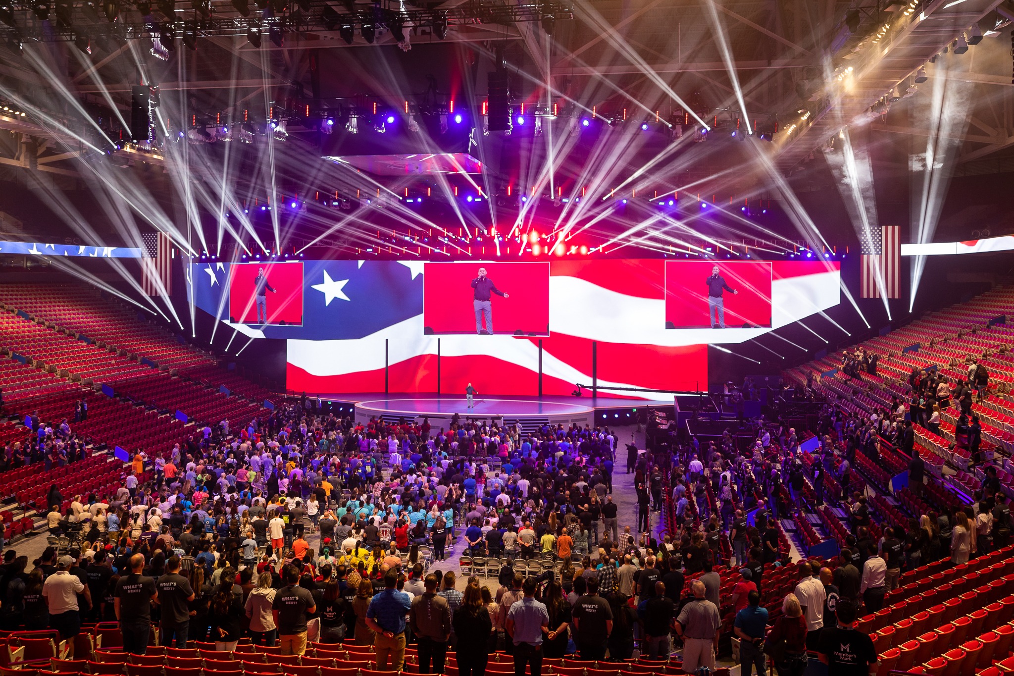 The Bud Walton Arena. A man speaks onstage with an American flag digital background. 