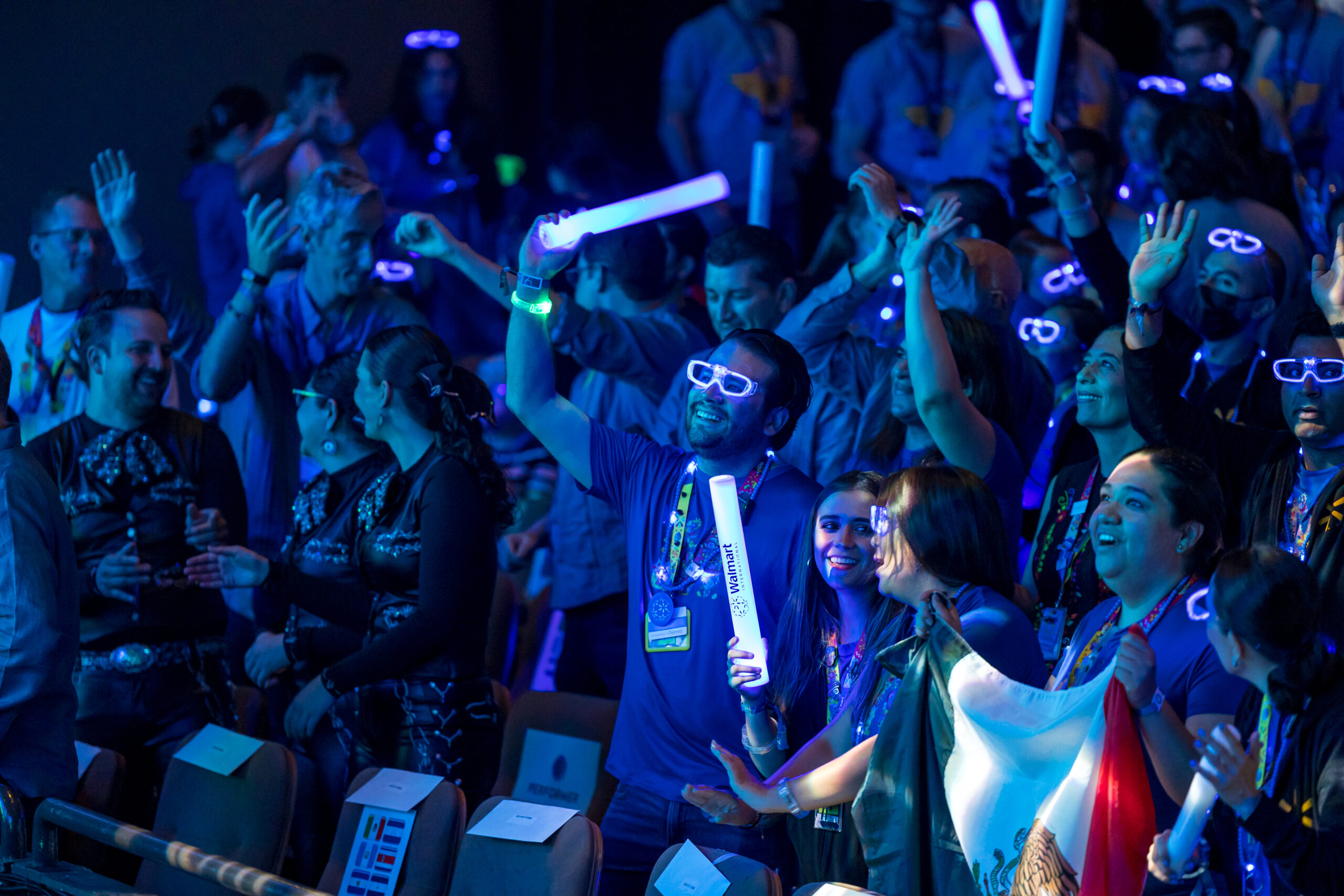 People in a crowd in the dark with glowing glasses and plastic tubes. The Wal-Mart logo is on the tubes.