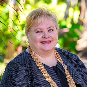 A portrait of Stephanie Lapsley. She is a blonde white woman with a thick gold necklace and dark jacket