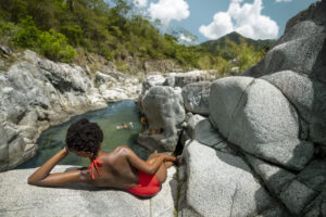 woman laying on large rock looking out at people swimming in lake