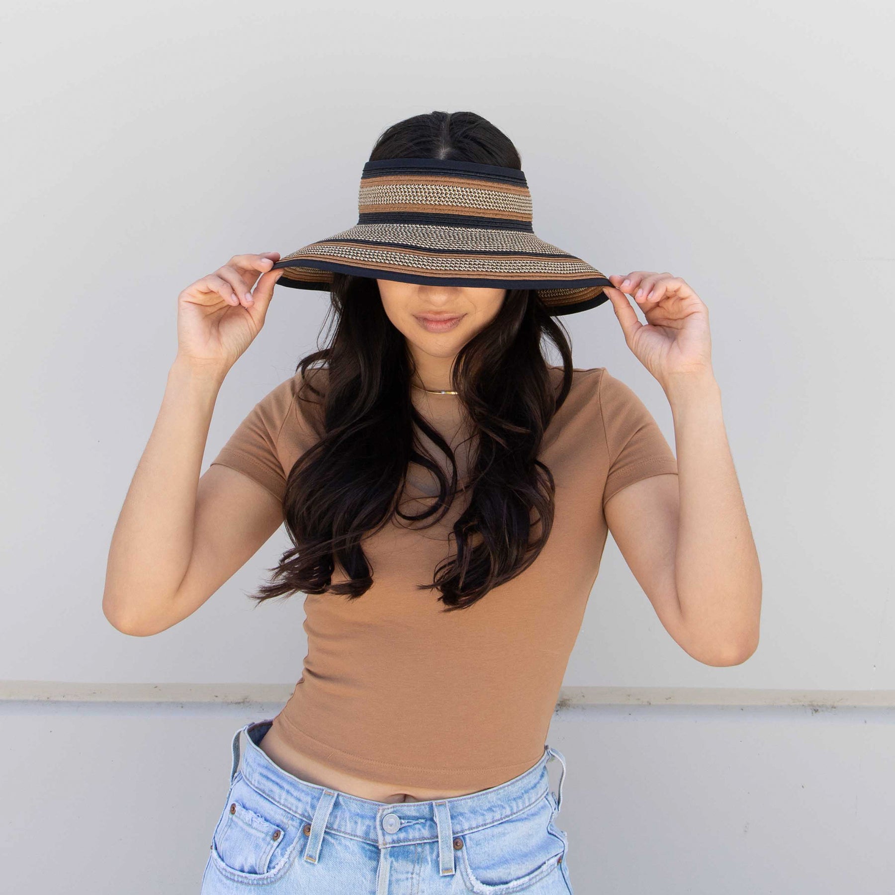 A woman modeling a dyed, close-knit straw hat with an open top. It has dark blue, brown and grey stripes.