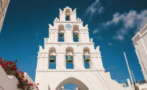 The top of a white church in Santorini with blue bells in a pyramid shape
