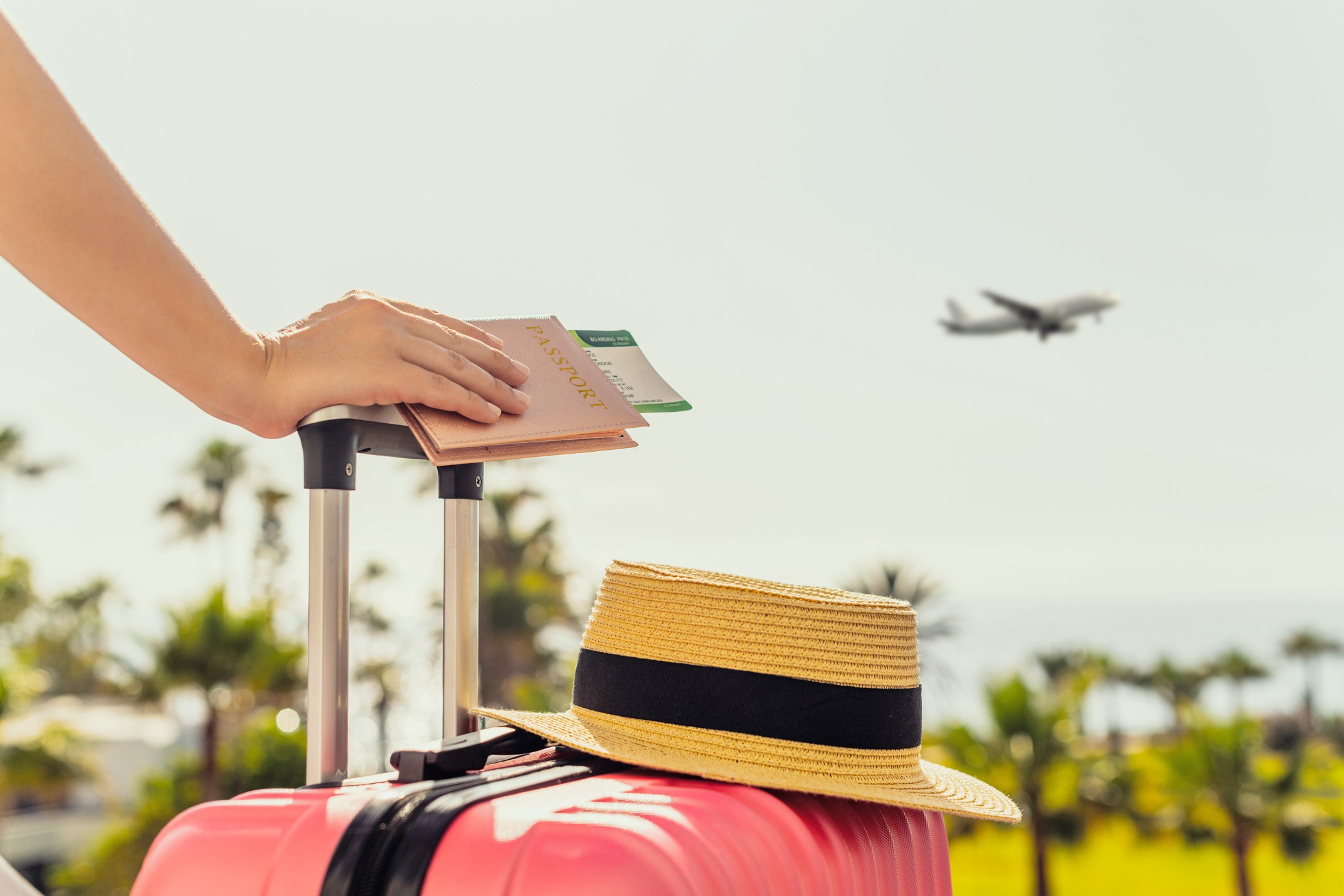 Woman with pink suitcase and passport with boarding pass standing on passengers ladder with plane in background