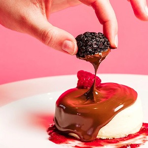 hand pulling blackberry from top of chocolate covered cheesecake at Bar 32 Chocolate