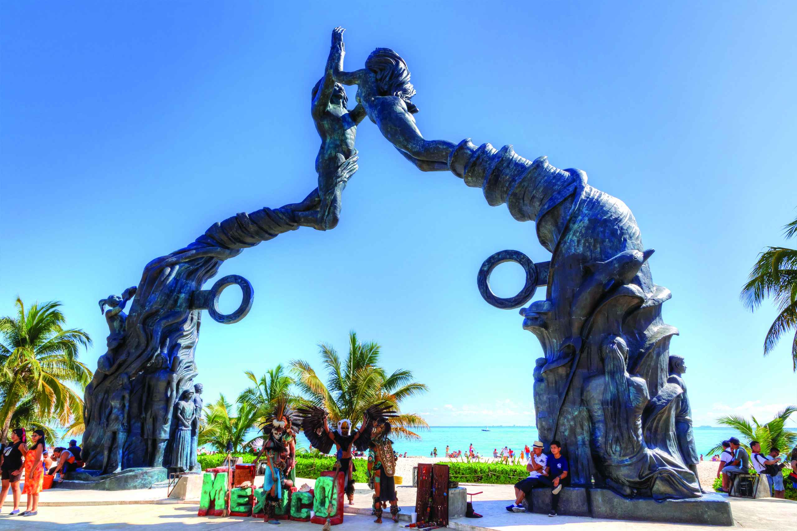 people posing for a picture dressed in aztec-themed attire in front of Fundadores Park beach at Playa del Carmen on the Caribbean coast of Riviera Maya