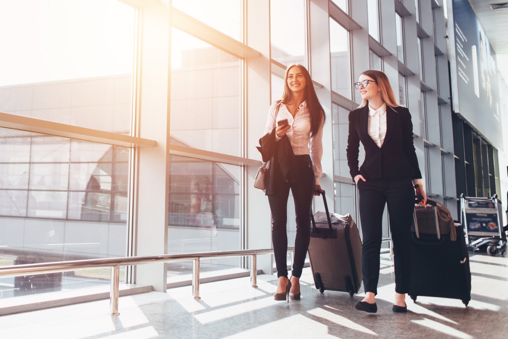 Two smiling business partners going on business trip carrying suitcases while walking through airport passageway