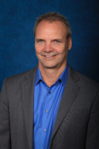 phil cooper wearing grey plazers and blue dress shirt