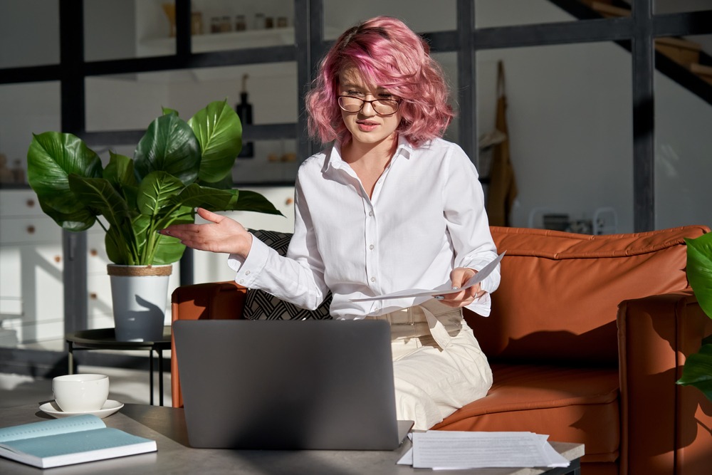 Young woman with pink hair communicating by webcam conference working from home office making online remote video call